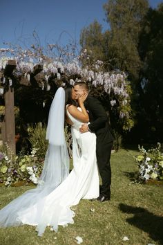 a bride and groom kissing in front of a flower covered arbor with purple flowers on it