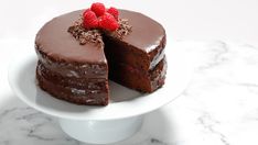 a chocolate cake with one slice cut out and topped with raspberries on a white plate