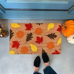 a person standing next to a door mat with fall leaves on it