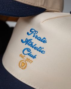 Pirate Athletic Club Script Hat Size: Adjustable Snap Cap Color: Cream/Navy Front Pirate Athletic Club Script Logo Embroidery Stitch Count: 7,398 Embroidery Color: Gold, Powder Blue, White Hat Cream, Embroidery Stitch, Athletic Club, Gold Powder, Athletic Clubs, Script Logo, Logo Embroidery, Powder Blue, Hat Sizes