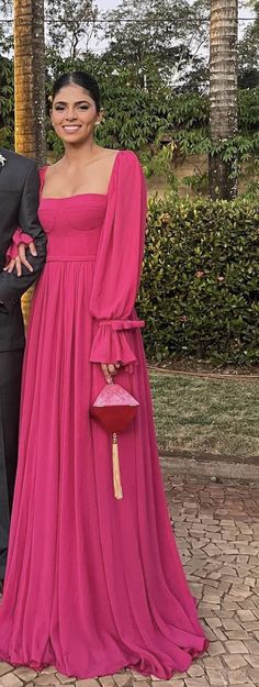 a man and woman standing next to each other in front of palm trees wearing pink dresses