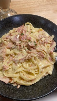 a plate of pasta with ham and cheese on it next to a glass of milk