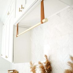 a bathroom with white cabinets and brown handles hanging from the wall next to a mirror