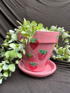 a pink planter with strawberries painted on the side and green leaves around it