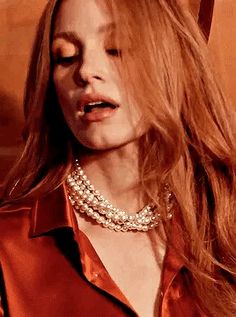 a woman with long red hair wearing a collared shirt and pearls on her necklace