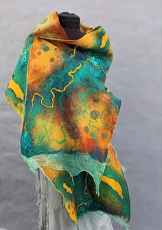 a colorful shawl draped over a wooden post by the water with yellow and green designs on it