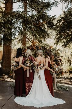 three women in long dresses standing next to each other with flowers on the back of their backs