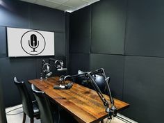 a wooden table topped with black chairs next to a microphone on top of a wall