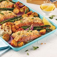 salmon, asparagus and potatoes in a blue casserole dish with lemon wedges