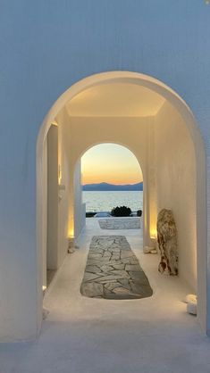 an archway leading to the ocean at dusk with lights on and a rug in between