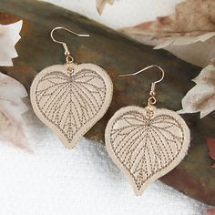 a pair of heart shaped earrings sitting on top of a leafy tree branch next to leaves