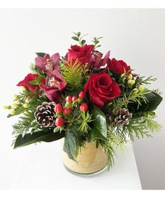 a bouquet of red roses and greenery in a wooden vase on a white table