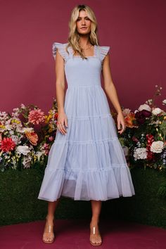 a woman standing in front of flowers wearing a blue dress with ruffles on it