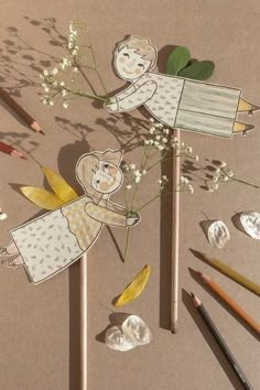 two paper angels on sticks with flowers and pencils