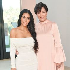 two women standing next to each other in front of a large window and one is wearing a white dress