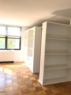 an empty living room with white bookcases and wood flooring in front of a window