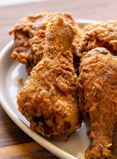 some fried chicken on a white plate sitting on a wooden table and ready to be eaten