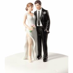 a bride and groom figurine standing next to each other on a white surface