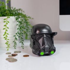 a star wars helmet sitting on top of a white desk next to coins and a computer