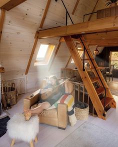 a woman sitting on a couch in a loft next to a stair case and window