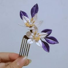 a hand holding a purple and white flower on top of a comb