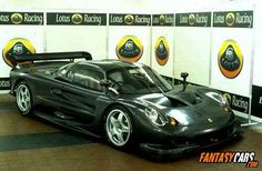 a black sports car parked in front of a wall with signs on it that read lotus racing