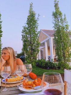 a woman sitting at an outdoor table with food and wine