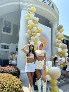 two young women standing next to each other in front of a building with balloons on it