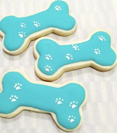 three decorated cookies with blue icing and white dog paw prints on them sitting on a table