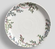 a white plate with holly and red berries painted on the rim is sitting on a gray surface