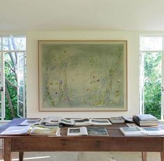 a table with many books on it in front of large windowed wall and trees