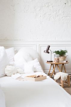 a bed with white sheets and pillows next to a small table with a potted plant on it