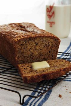 there is a loaf of bread with butter on the cooling rack next to a cup