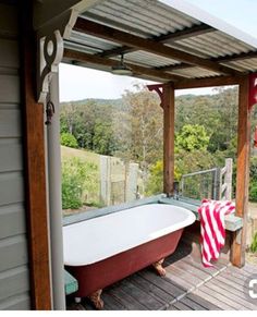 an old fashioned bathtub on a deck with a red and white towel draped over it