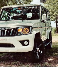 the front end of a white four door suv parked in grass with trees behind it