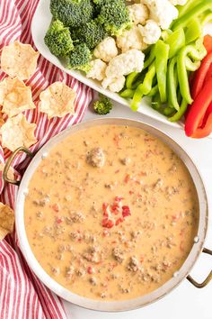 a white bowl filled with soup next to vegetables and crackers on a red and white towel