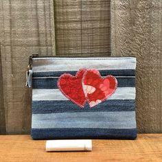 a blue and white striped purse with two red hearts on the front, sitting on top of a wooden table