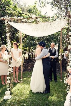 a bride and groom are hugging under an outdoor chute with white flowers on it