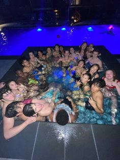 a large group of people in a pool with blue lights on the side and one person taking a photo