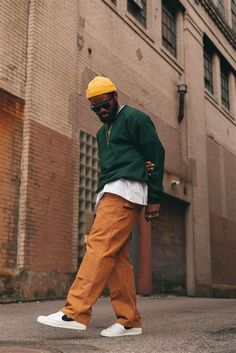 a man walking down the street wearing an orange hat and green jacket with white sneakers