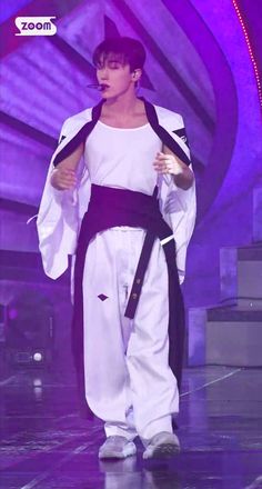 a male in a white shirt and black belted pants on a stage with purple lighting