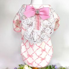 a pink and white dress with a bow on the front is sitting next to flowers