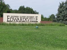 a sign for the university of edwardsville in front of some trees and grass with a blue fire hydrant