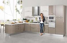 a woman standing in the middle of a kitchen with stainless steel appliances and cabinets,