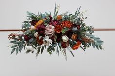 an arrangement of flowers and greenery hanging from a bar in front of a white wall