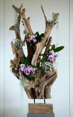 a wooden sculpture with flowers and plants on it's base in front of a white wall