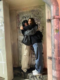 two people hugging each other while standing in front of graffiti covered walls and doorways