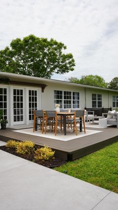 a patio with chairs, table and couches in front of a white house on a sunny day