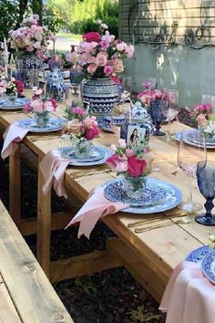 an outdoor table set with blue and white plates, pink flowers and vases on it