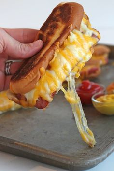 a person holding a hot dog with cheese and bacon